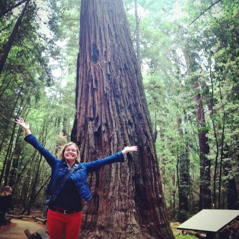 Becky beneath a redwood with arms outstretched